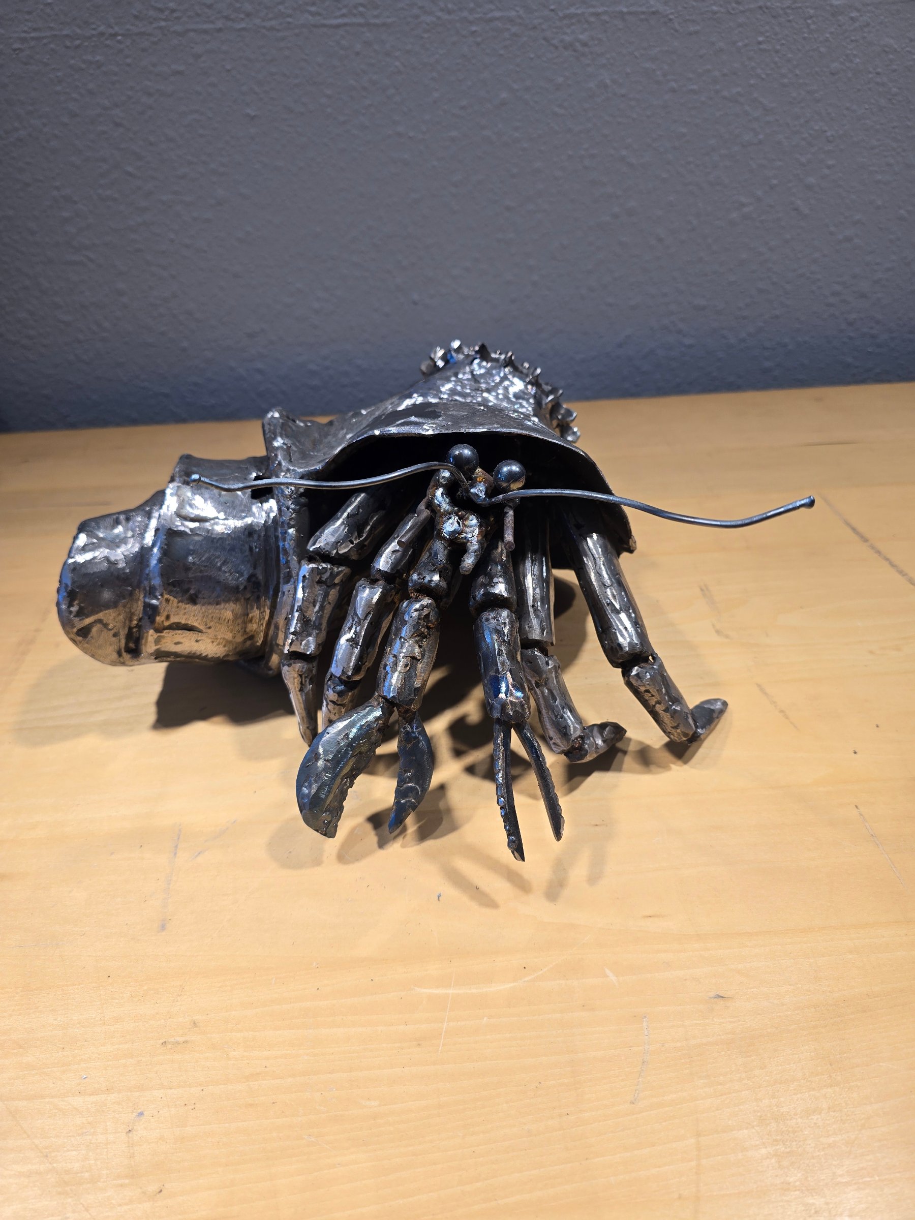 Welded steel hermit crab sculpture with raw patina, claws, antennae, and spiral shell.