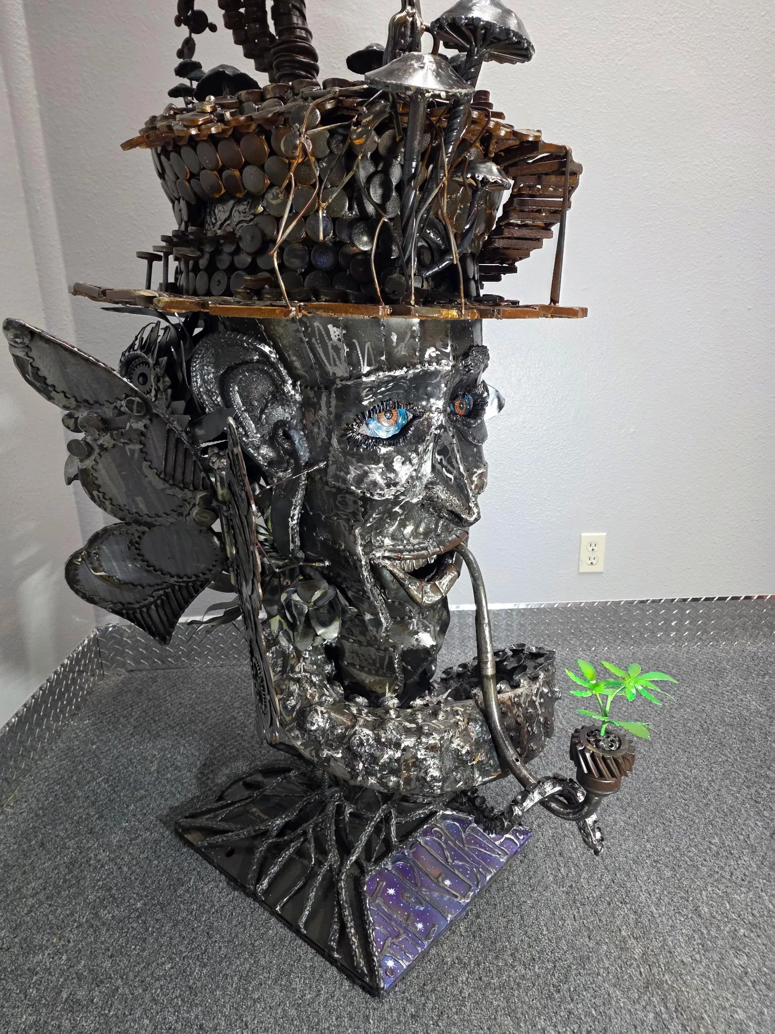 Carbon steel face sculpture with pipe, top hat, dragonfly wings, and glowing eyes.