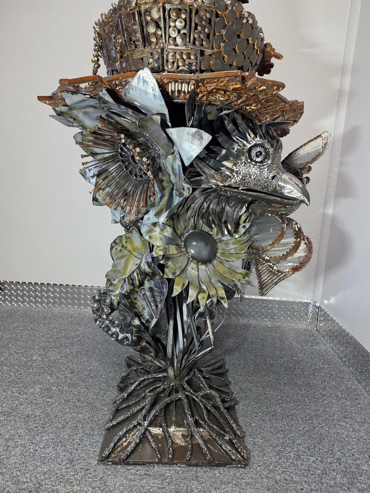 Welded carbon steel sculpture of a bird amid flowers, wearing a bolt-covered top hat.