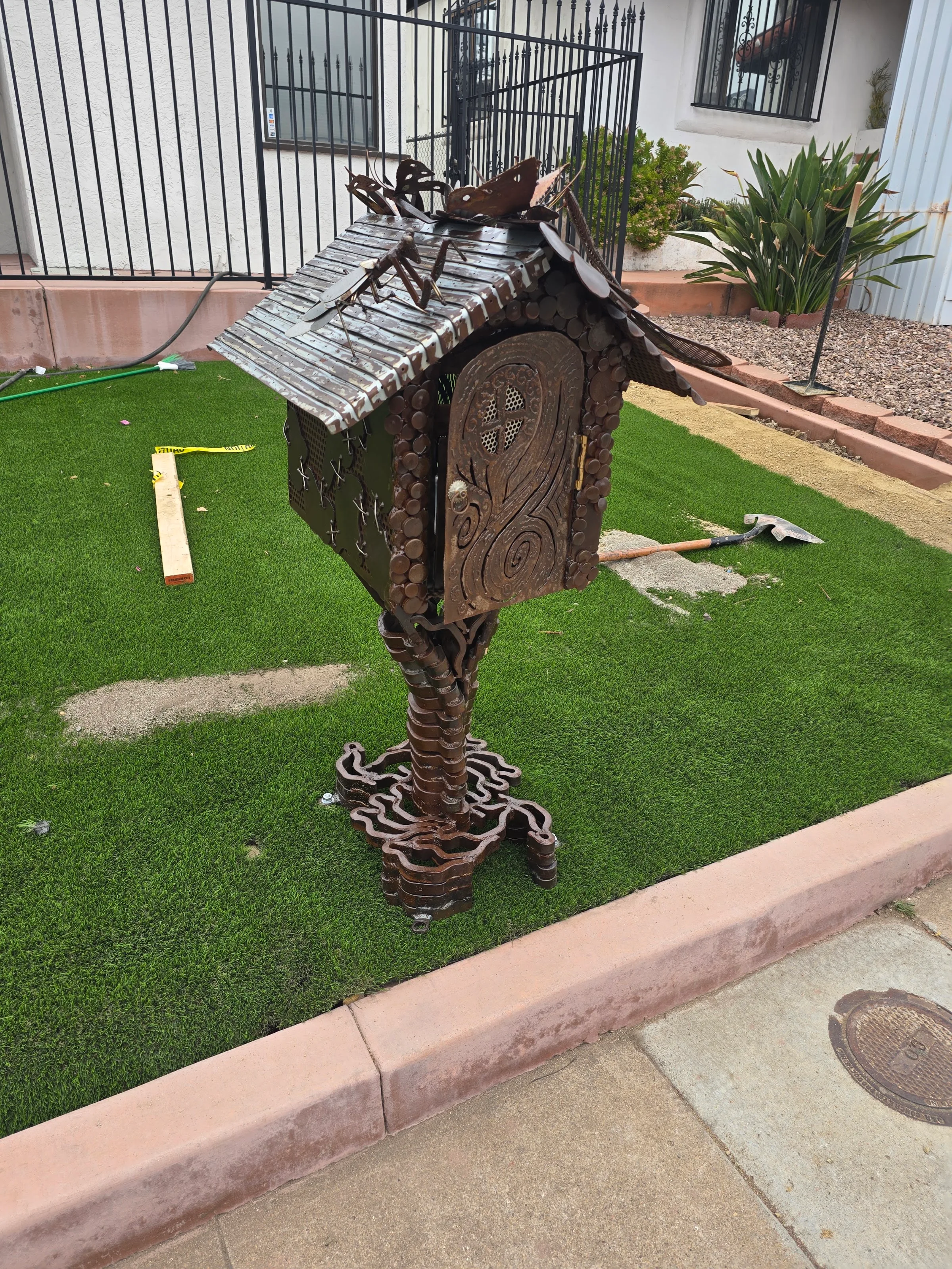 Handcrafted steel mailbox sculpture with patinated finish, decorative door, coin accents, and butterfly topper.
