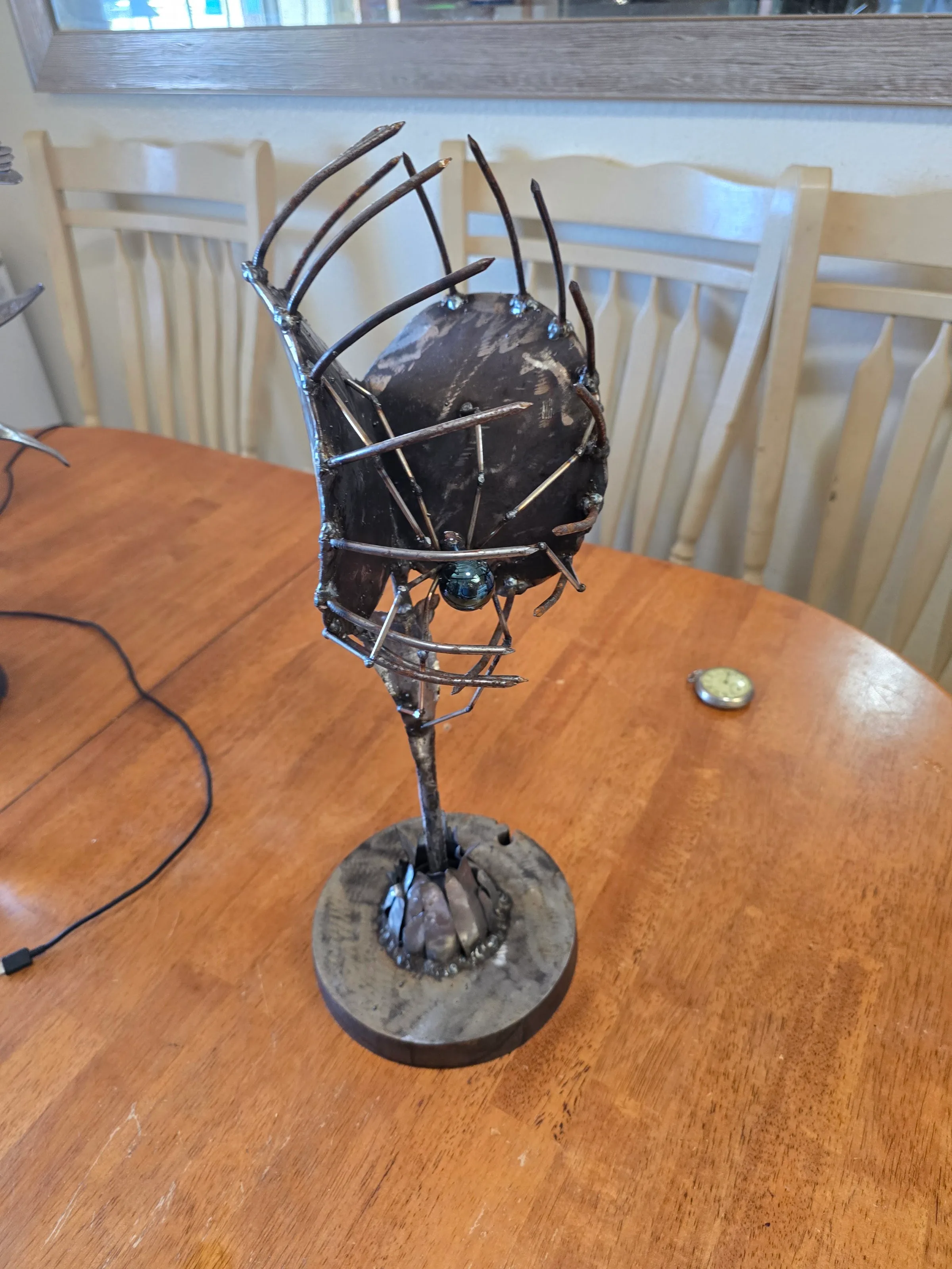 Welded steel Venus flytrap sculpture with spiked jaws, glass eye, on a round base.